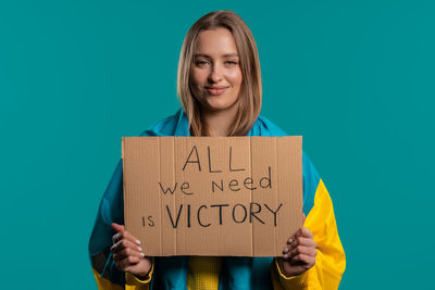 Portrait of young woman holding card while standing against blue background