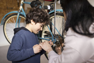 Smiling boy tightening screw of bicycle wheel with mother at recycling center