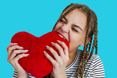 Teenage girl biting heart shape against blue background