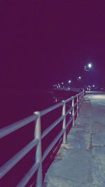 Illuminated railing by sea against clear sky at night