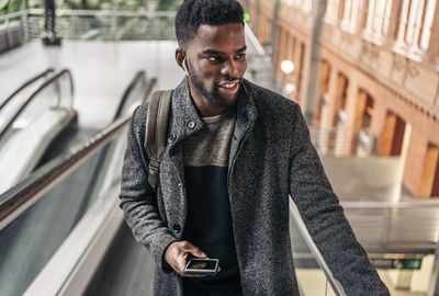 Smiling man using mobile phone standing on escalator