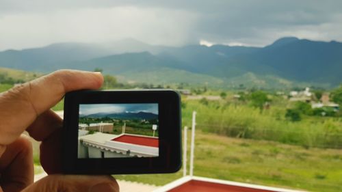 Hand holding smart phone against mountain range