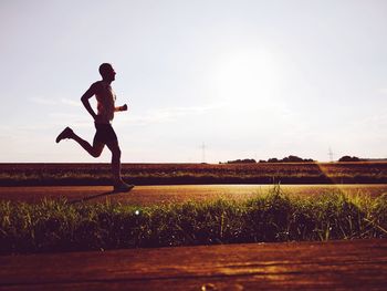 Side view of man running on field against sky during sunny day