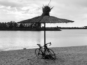 Monochromatic photo of a bicycle sitting near a thatched food umbrella on the beach