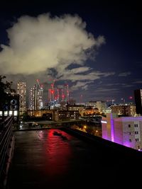 Illuminated buildings by river against sky in city at night