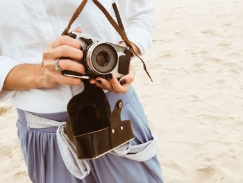 Midsection of woman holding old-fashioned camera at beach