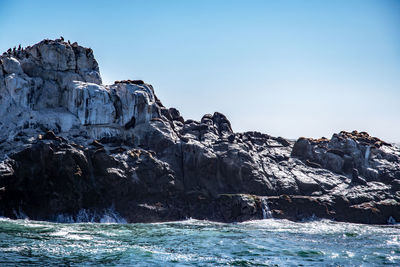 Rock formation in sea against clear sky