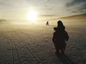 Rear view of child on snow against sunset