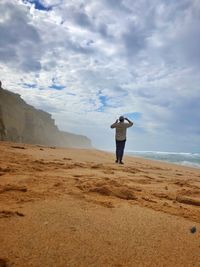 Rear view of man standing at beach against sky