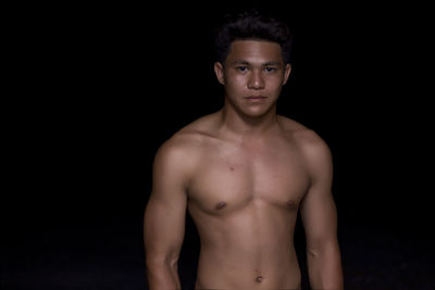 Portrait of shirtless bodybuilder standing against black background