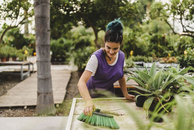 Female owner cleaning dirt with brush at nursery