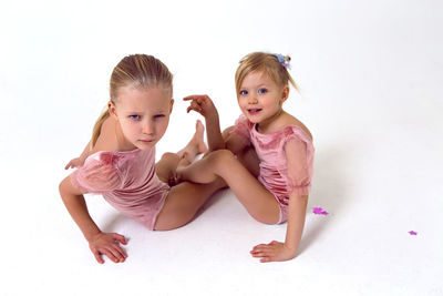 Two sisters sitting on a white background in pink bodysuits