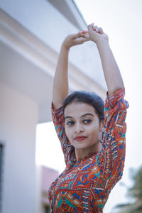 Smiling young woman looking away with arms raised