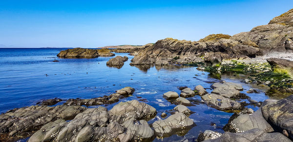 Rock formations on shore against clear blue sky