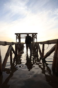 Rear view of men on pier over lake against sky during sunset