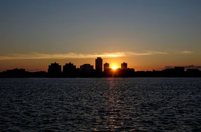 Silhouette buildings by sea against sky during sunset