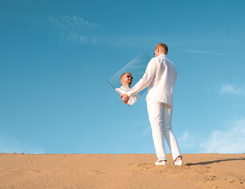 Full length of man standing on sand against clear blue sky