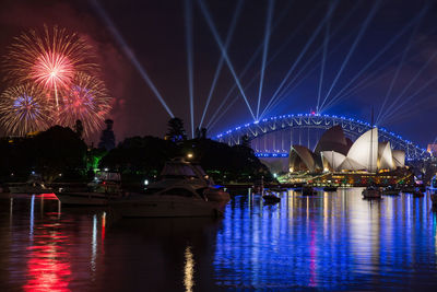 Illuminated firework display over river against sky at night