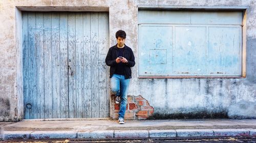 Full length of young man standing against old door with a phone 