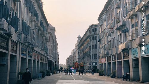 People walking on road amidst buildings against sky