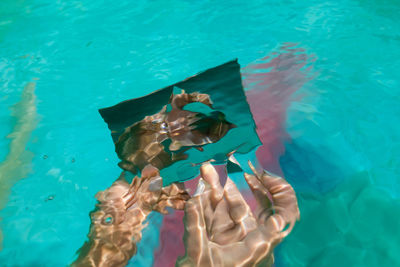 Cropped hands of woman holding mirror in swimming pool