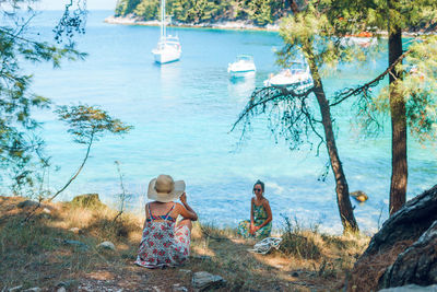 People sitting on shore against trees