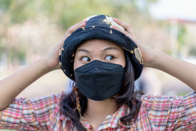 Young woman wearing medical surgical mask worries about her face and forehead has blackhead pimple 