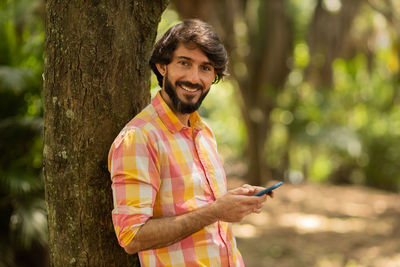 Young man with smartphone at day time with a green park in the background. mobile phone, technology,