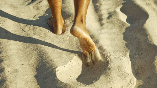 Low section of man with shadow on sand at beach