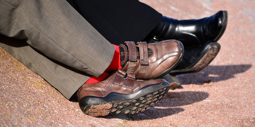 Low section of men wearing shoes sitting on sand