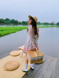 Woman wearing hat while standing by basket on lake