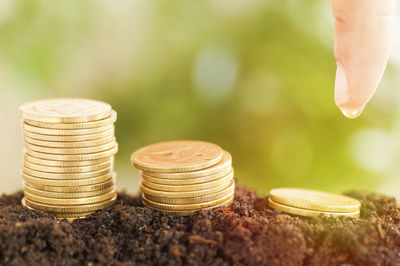 Close-up of cropped hand with water drop by coins on dirt