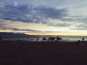 People on beach against sky during sunset