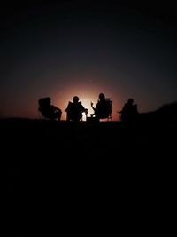 Silhouette people sitting on land against sky during sunset