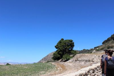 People on rocks against clear blue sky