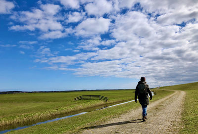 Rear view of woman walking along pastures under a blue clouded sky