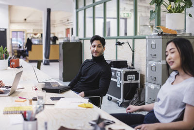 Smiling young man looking at female colleague in creative office