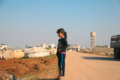 Side view of woman standing on road against clear sky