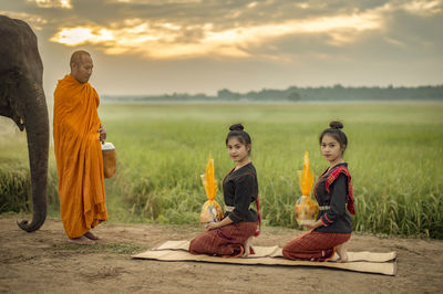 Full length of monk with people and elephant on field during sunrise
