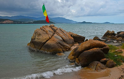 Pan-african flag on rock at shore against cloudy sky