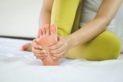 Low section of woman suffering from pain on leg sitting on bed at home