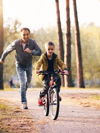 Full length of father and son riding bicycle in forest