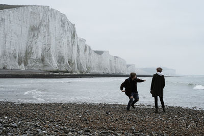 Rear view of man and woman walking on rock against sky