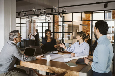 Female entrepreneurs discussing while sitting with male colleagues at desk in creative office