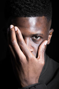 Close-up of young man drinking water against black background