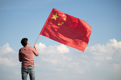 Rear view of man holding chinese flag standing against sky