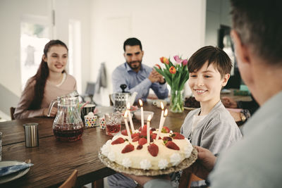 Boy looking at birthday cake while sitting with family at home