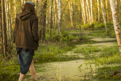 Rear view of woman walking in swamp against trees at forest