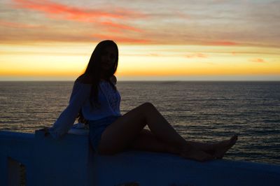 Woman sitting on beach at sunset