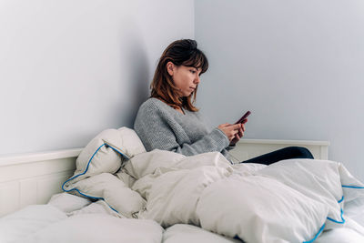 Young woman using mobile phone while sitting on bed at home